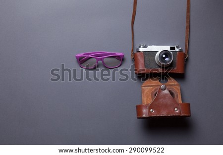 purple glasses and retro camera in leather case lying down on grey background
