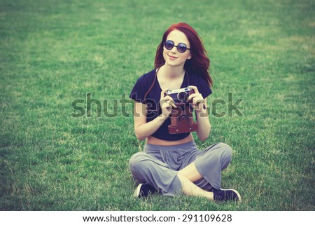 Young girl in indie style clothes with retro camera on green grass in the park