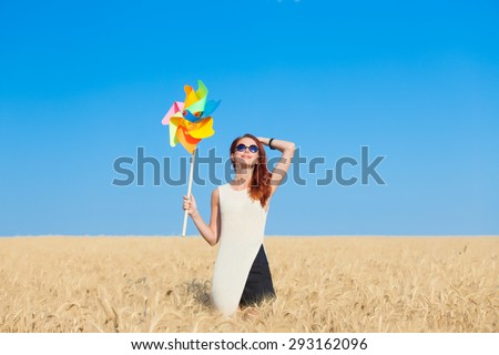 Redhead girl in white dress and wind toy at wheat field.