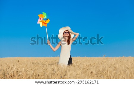 Redhead girl in white dress and wind toy at wheat field.