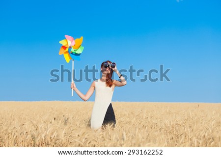 Redhead girl in white dress with binocular and wind toy at wheat field.