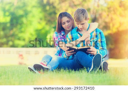 Young teen couple with notebook on the green grass in the park.