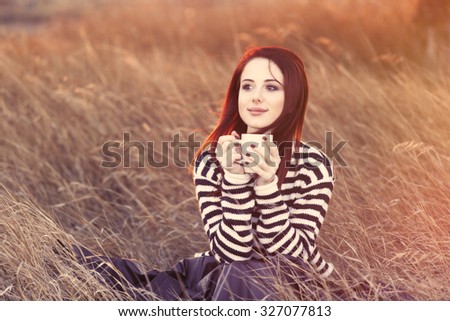 Woman with cup of tea or coffee sitting on the grass in autumn time