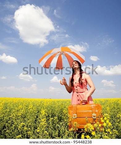 Brunette enchantress with umbrella and suitcase at spring rapeseed field.