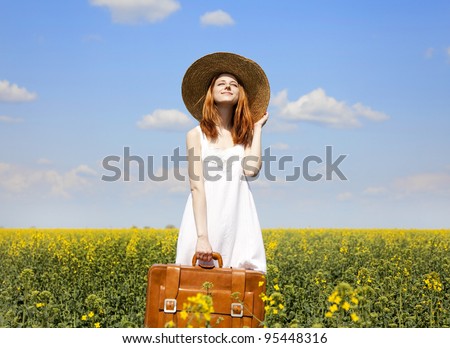 Redhead enchantress with suitcase at spring rapeseed field.