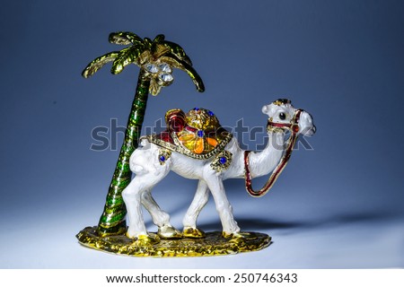 Small metal statue of camel with palm on yellow base with dark background