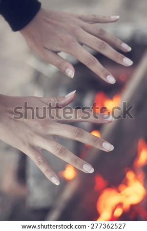 Girl warming his hands at campfire in forest