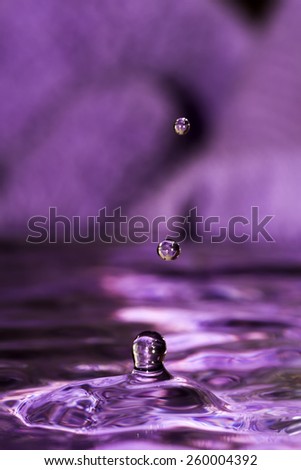 Water splash with two falling drops on dark purple background.
