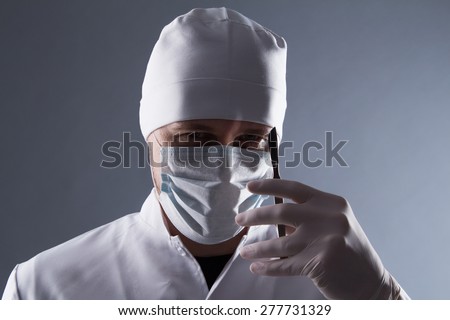 Male doctor in cap, mask and rubber medical gloves holding scalpel.