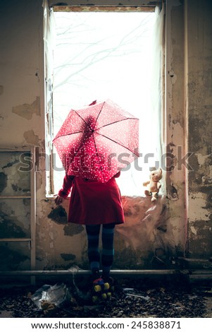 A young woman looks with a red coat and red umbrella out the window