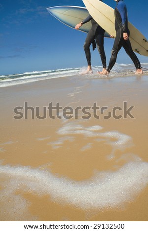 Two  males walking along the beach carrying surf boards