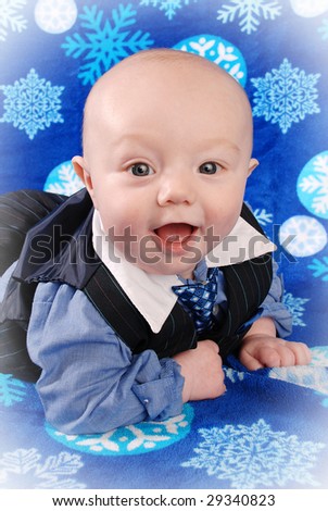 Smiling blue eyed 5 month old boy wearing a suit and tie. Taken on a blue blanket with white snowflakes.