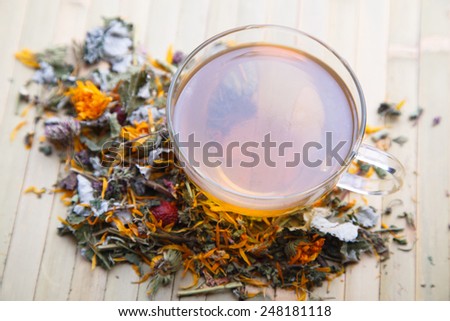 Scattered herb with dry yellow flower on bamboo and transparent mug with herbal tea