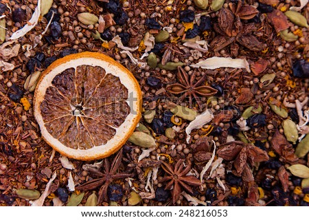 Texture of rooibos tea with dry anise, raisins, cardamom and ginger with dry orange slice on the left