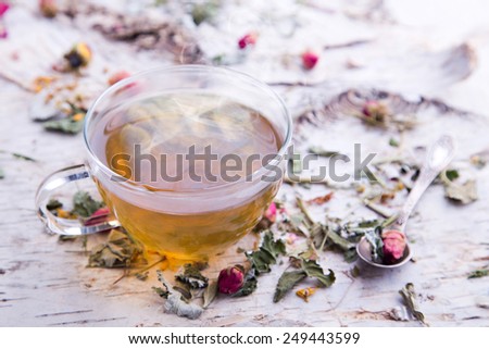 Transparent hot cup of herbal tea with dry rose on the beautiful texture of birch bark