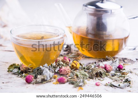 Transparent hot cup and teapot with herbal tea and dry roses and petals on the tree bark