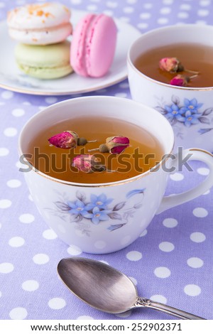 Two cups of herbal roses tea on lilac polka dots towel with spoon and three colorful macaroons on the dish background