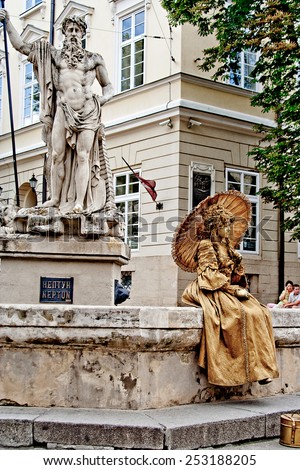 LVIV, UKRAINE - JUNE, 29: Gold living statue of woman sitting under the statue of Neptunus, June 29, 2013