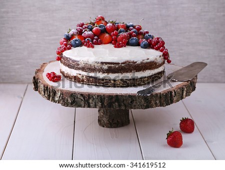 Home made Earl Grey cake with cream cheese and berries and mashed strawberries in brandy inside, on wooden cut cake stand on white wood table