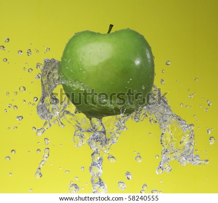 Green apple in water splashes on yellow background