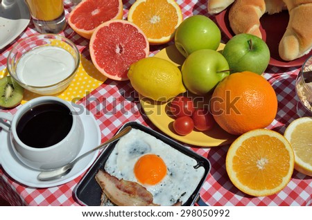 Breakfast or brunch with cup of fresh coffee, ham and eggs, Greek yogurt, cereals, croissants and colorful fruits served on red-white tablecloth