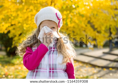 Girl child with cold rhinitis on autumn background, flu season, allergy runny nose.