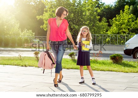 Mom and schoolgirl of primary school holding hands. The parent takes the child to school. Outdoors, return to the concept of the school
