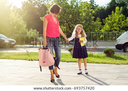 Mom and pupil of elementary school  holding hands. The parent takes the child to school. Outdoors, return to the concept of the school.