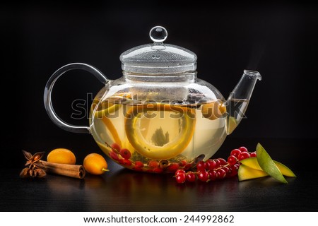 Teapot with fruit tea. Tea with natural fruits in clear glass teapot on black background