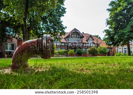 Old hydrant in the garden in the village center. Green grass and old houses out of focus on the background