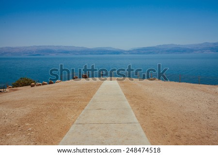 Straight path on a rocky beach leading to the sea with distant mountains