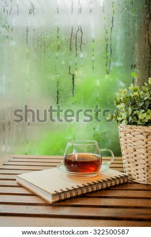 Cup of hot tea and book on a wooden ,water drops on a window glass after the rain.
