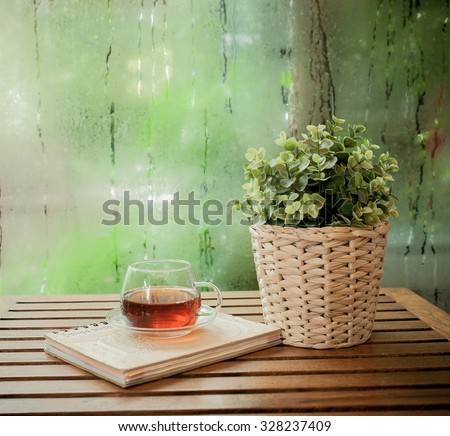 Cup of hot tea and book on a wooden ,water drops on a window glass after the rain.