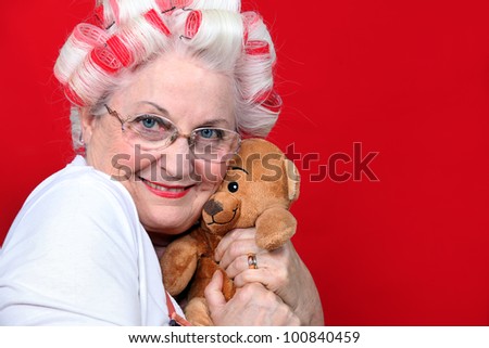 An old woman with hairroller on hugging a teddy bear.