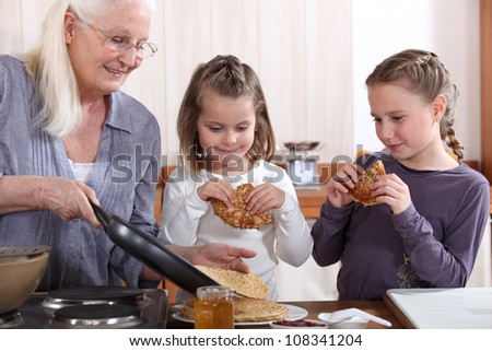 A grandmother cooking crepes for her granddaughters.