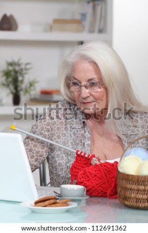Elderly lady knitting by laptop