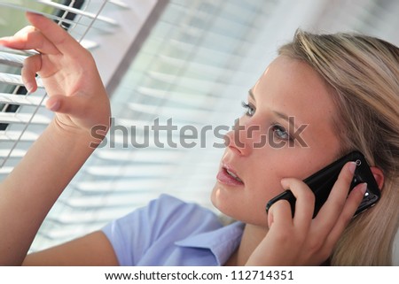 Woman on the phone looking through venetian blinds