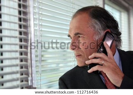 Senior businessman looking through blinds whilst making call