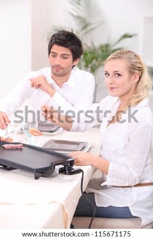 Couple cooking meat on a tabletop electric plate