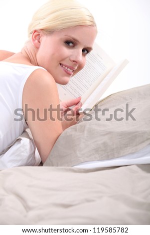 Young blond woman reading a book on her bed