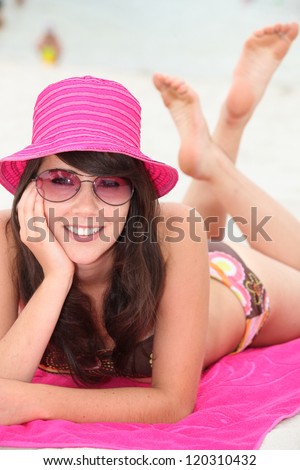 Young woman lying on the beach in  bikini and a bright pink hat