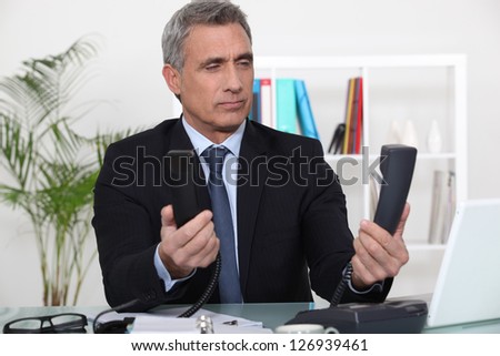 Over worked businessman holding two telephones