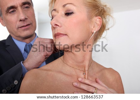 Man attaching necklace to wife\'s neck
