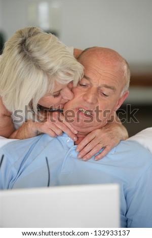 mature lady kissing her husband browsing with laptop