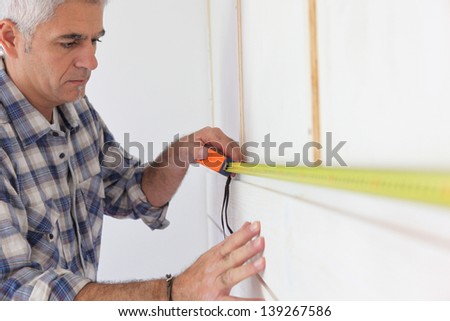 Grey haired handyman measuring wall