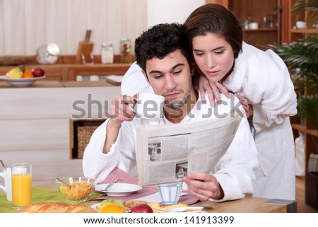 Young couple reading a newspaper at breakfast