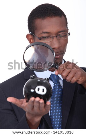 black well dressed man watching a piggy bank with a magnifying glass