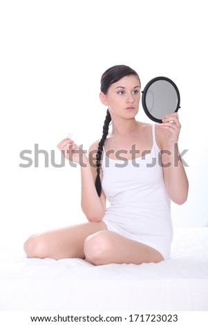 Young woman sat on bed holding mirror