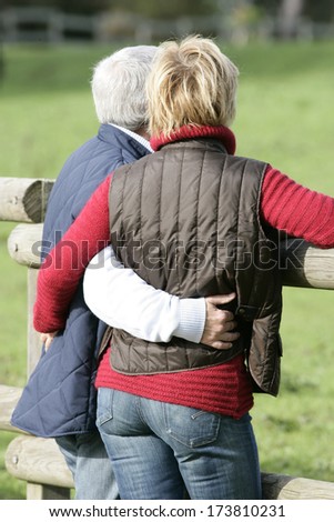 Married couple hugging by wooden fence