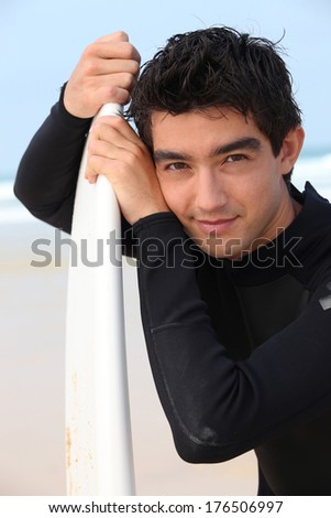 Young man in wet suite stood with surfboard